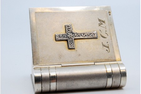 Caixa de comprimidos em prata em forma de livro de orações com interior dourado e tampa basculante.